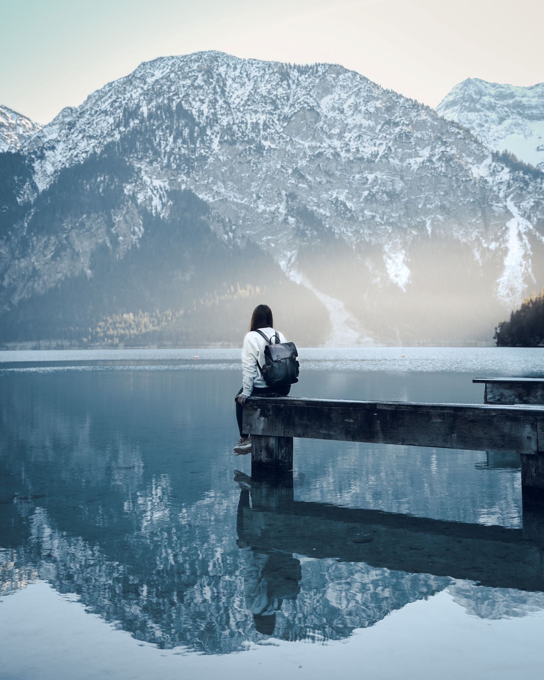 Frau mit Rucksack sitzend auf einem Holzsteg über einem See