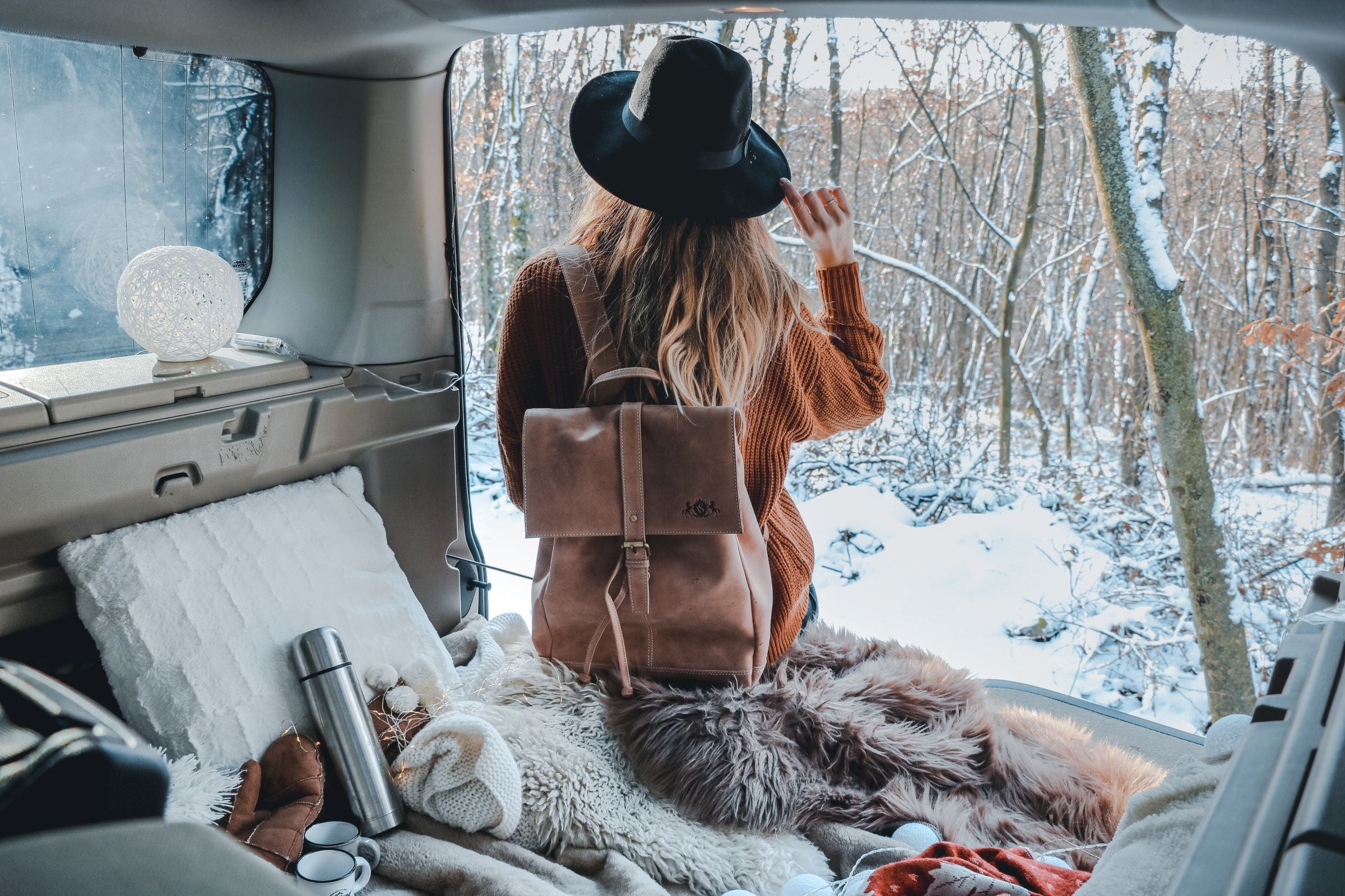 Frau mit Rucksack sitzend im geöffneten Kofferraum eines Buses.